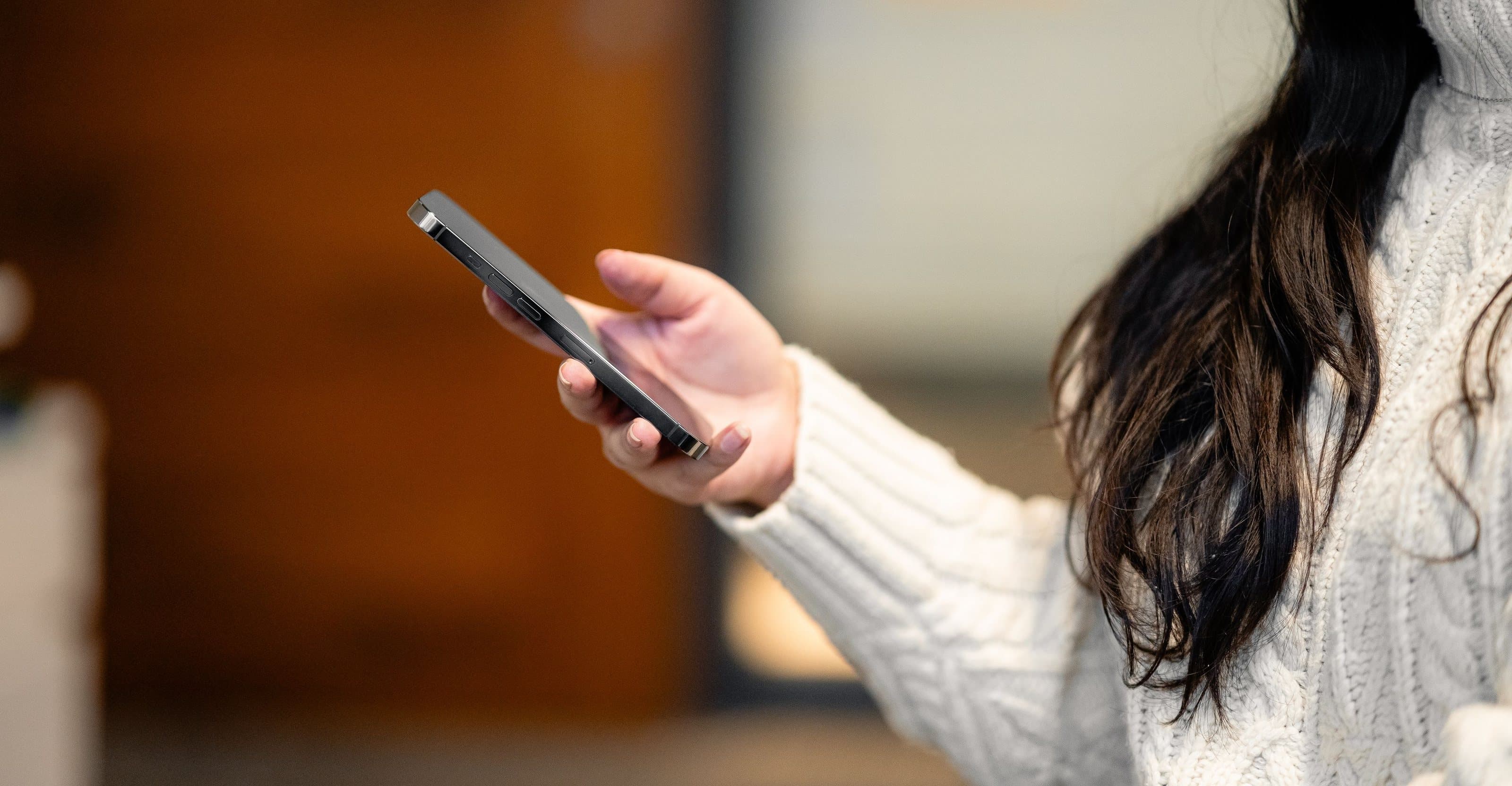 A hand holding a phone in a warm, bright room